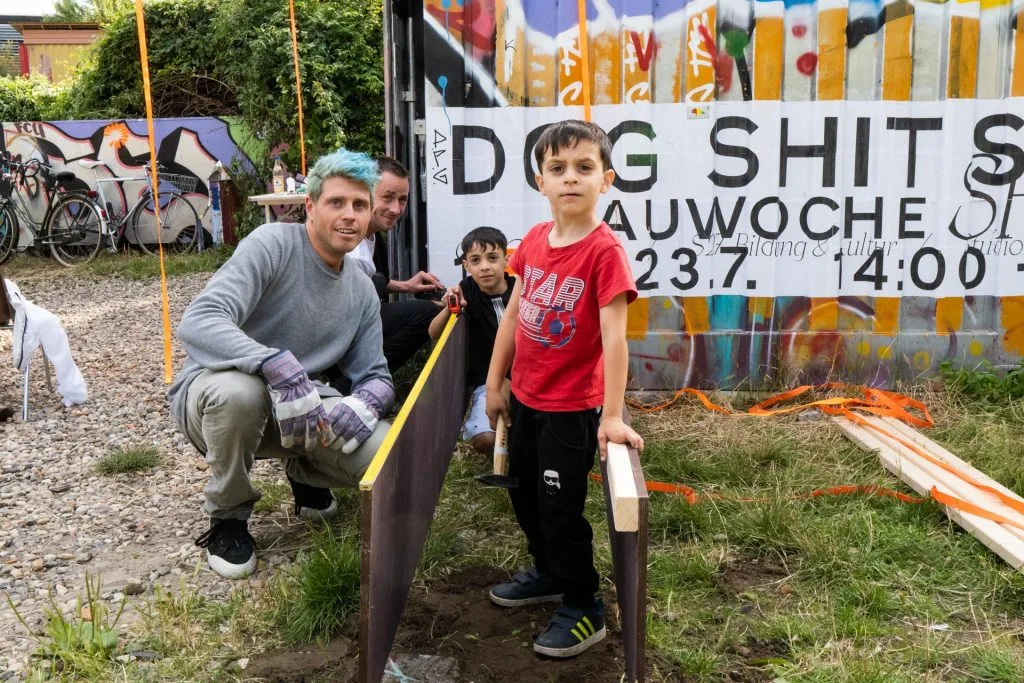 DogShitSpot — Gruppe vor dem Bauwoche-Schild am Container
